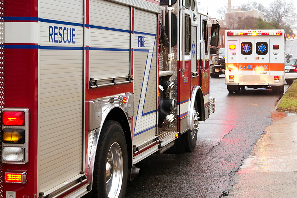 Two ambulances arrive at the scene of an accident. A car being towed can be seen in the background.