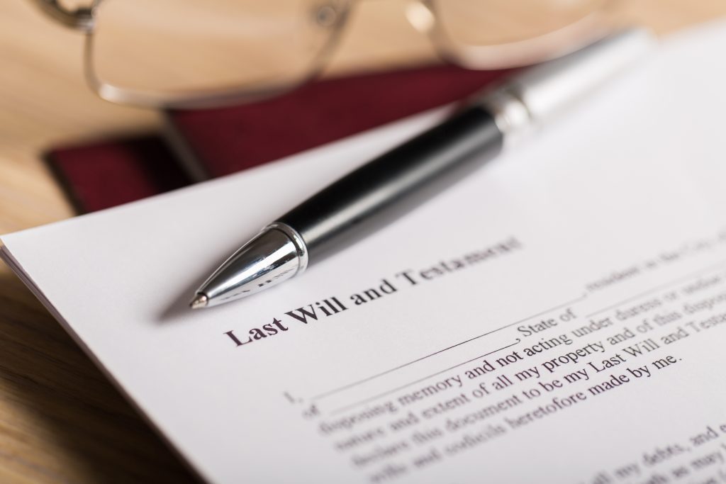 A black pen sits on top of a blank last will and testament, which rests next to a pair of reading glasses