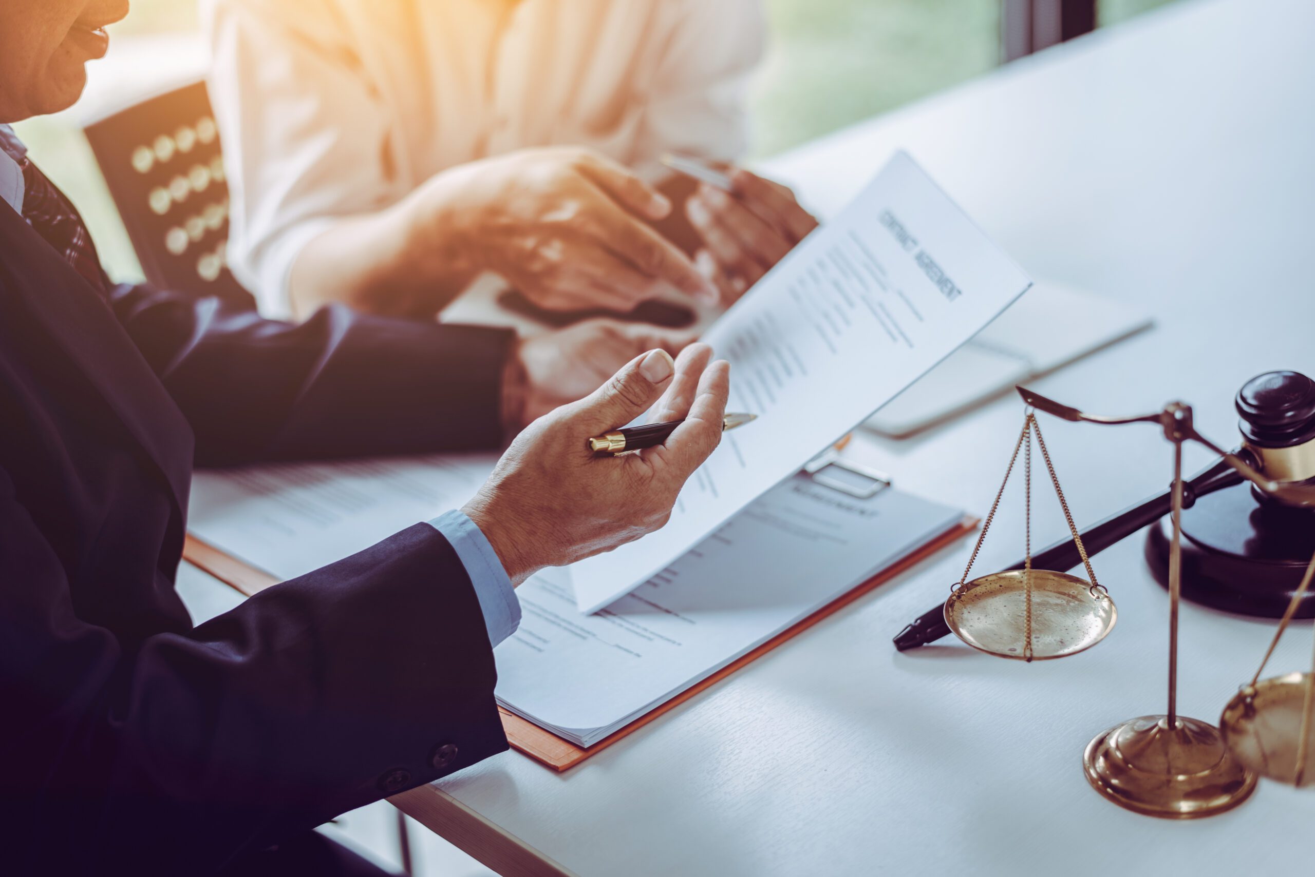 A lawyer holding a pen reviews a contract with a businessperson.