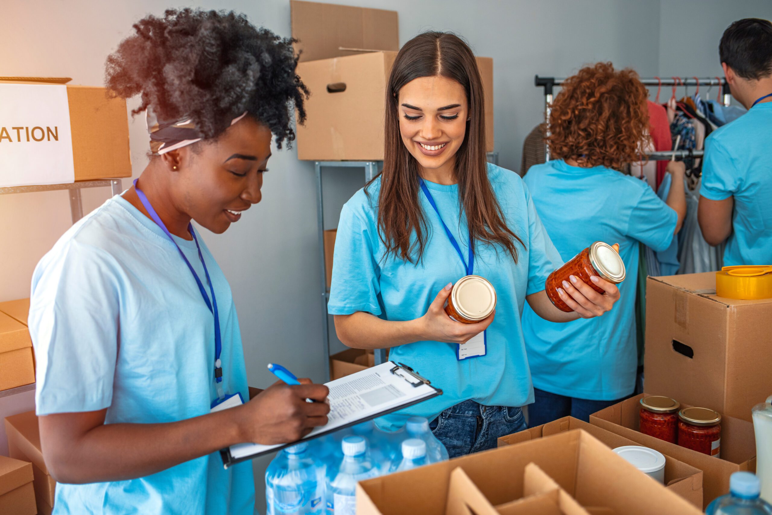 A group of four people sort through food and clothing donations with smiles on their faces.