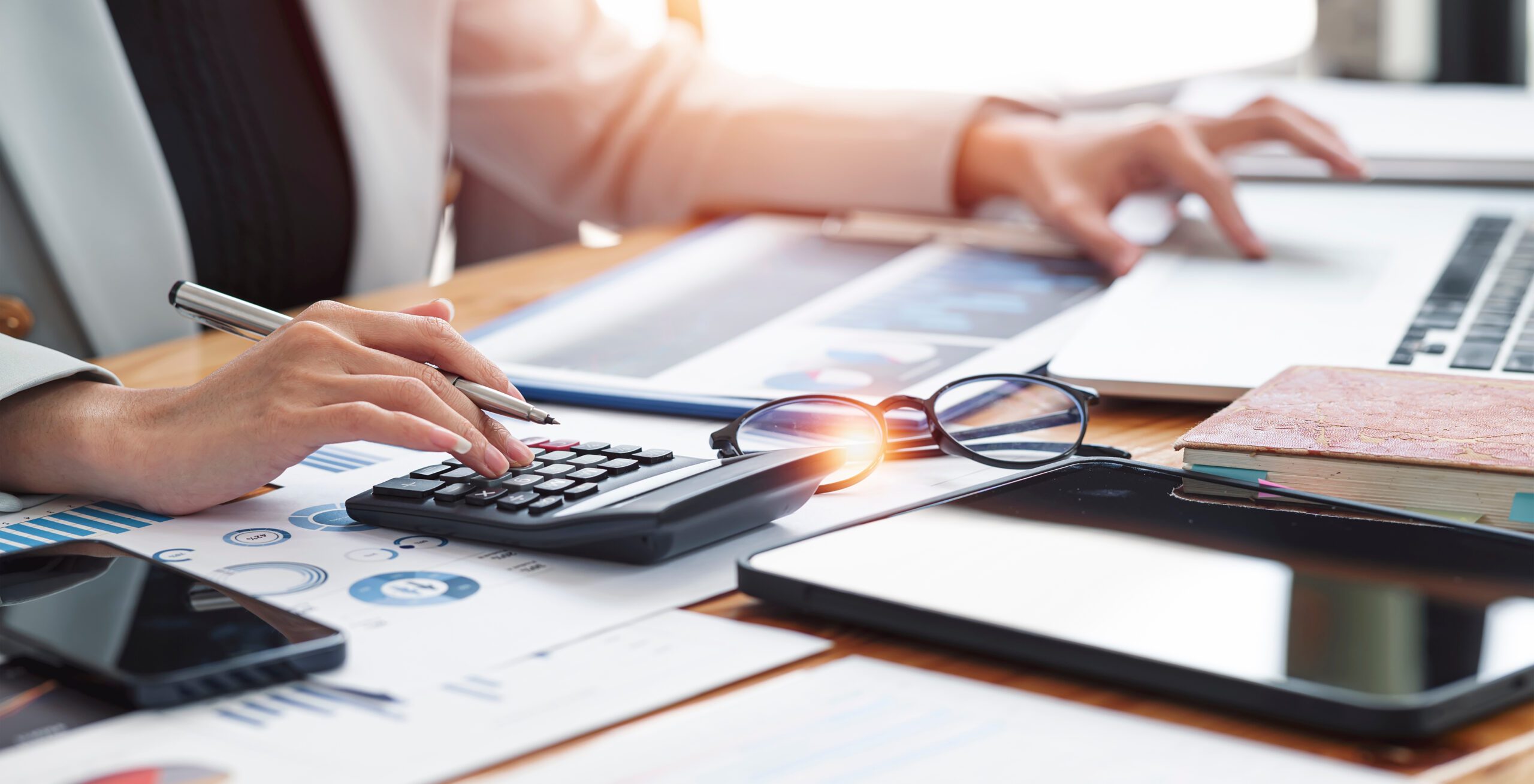 A person is working on a computer with their left hand and a calculator with their right hand.