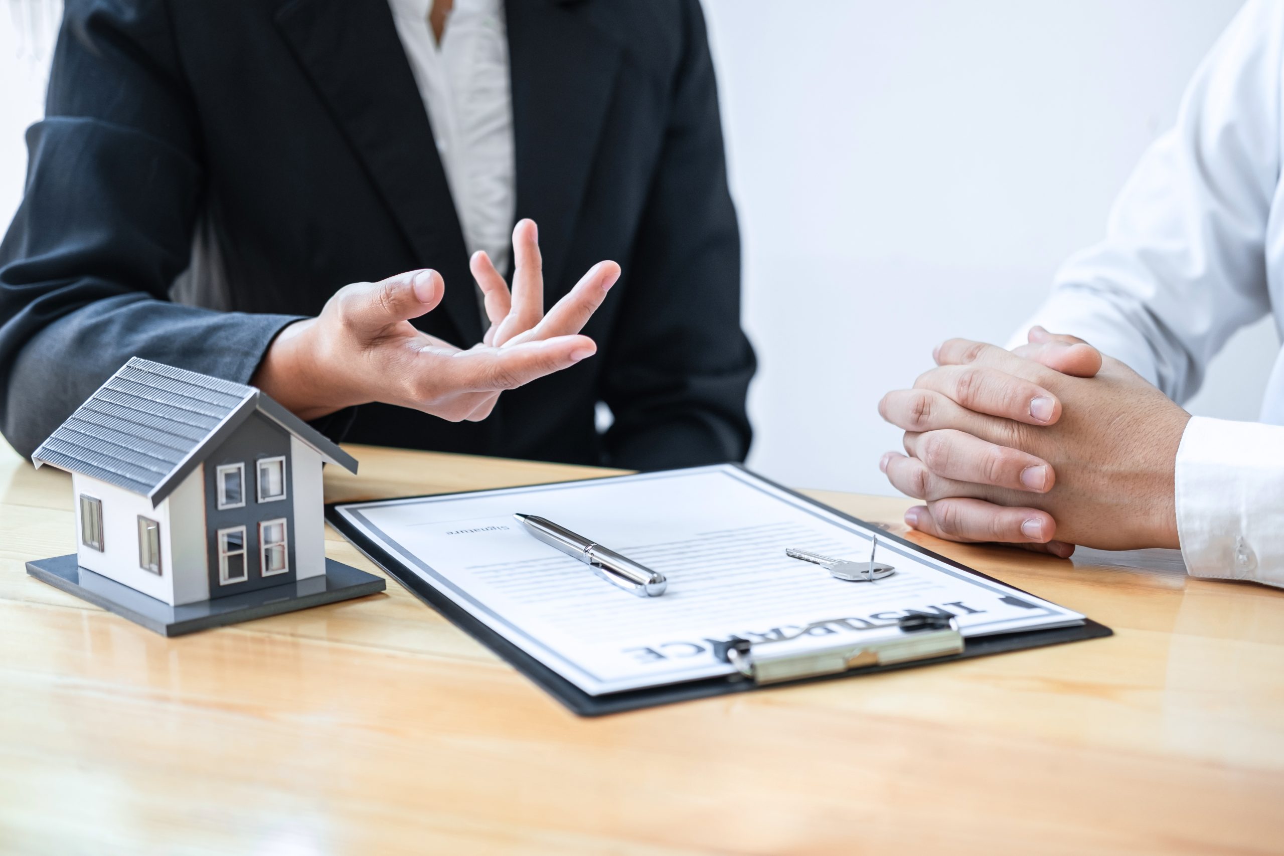 Two people discussing paperwork on a clipboard with a small house on the desk next to them.