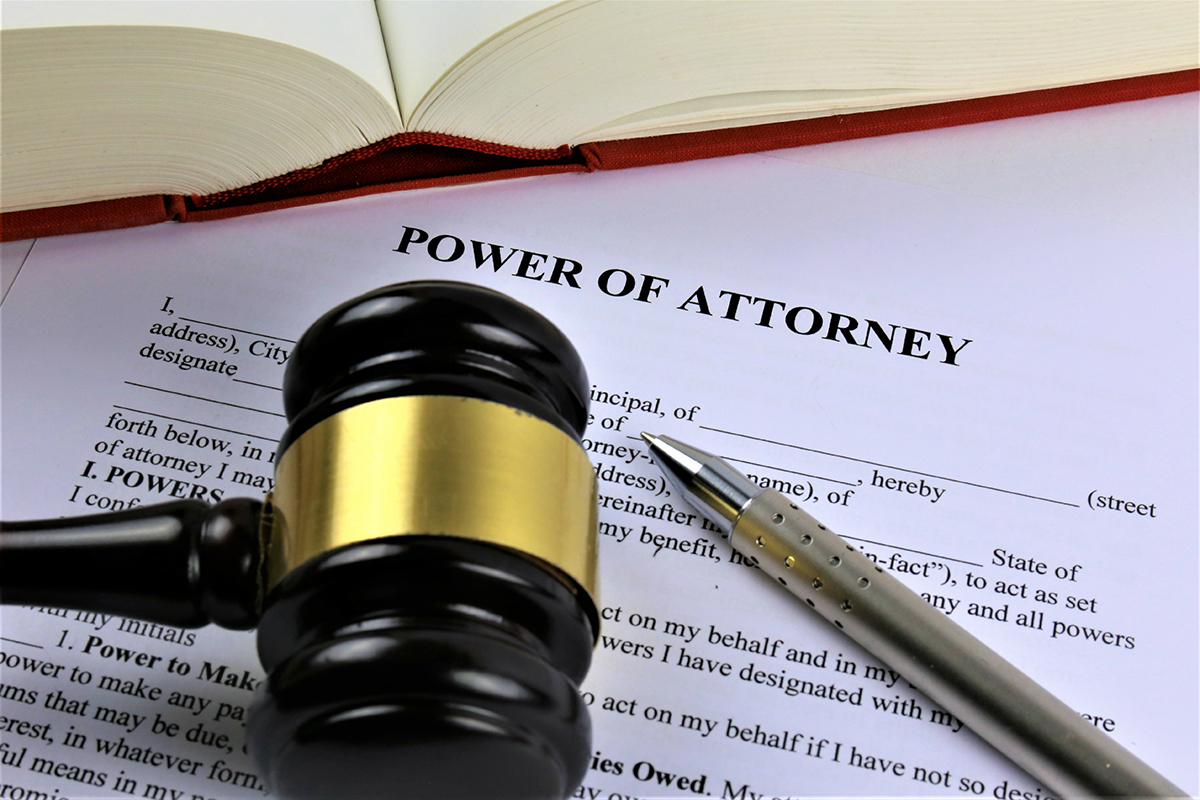 An open book, a gavel, and a pen rest on top of a paper that is a draft of a power of attorney document.