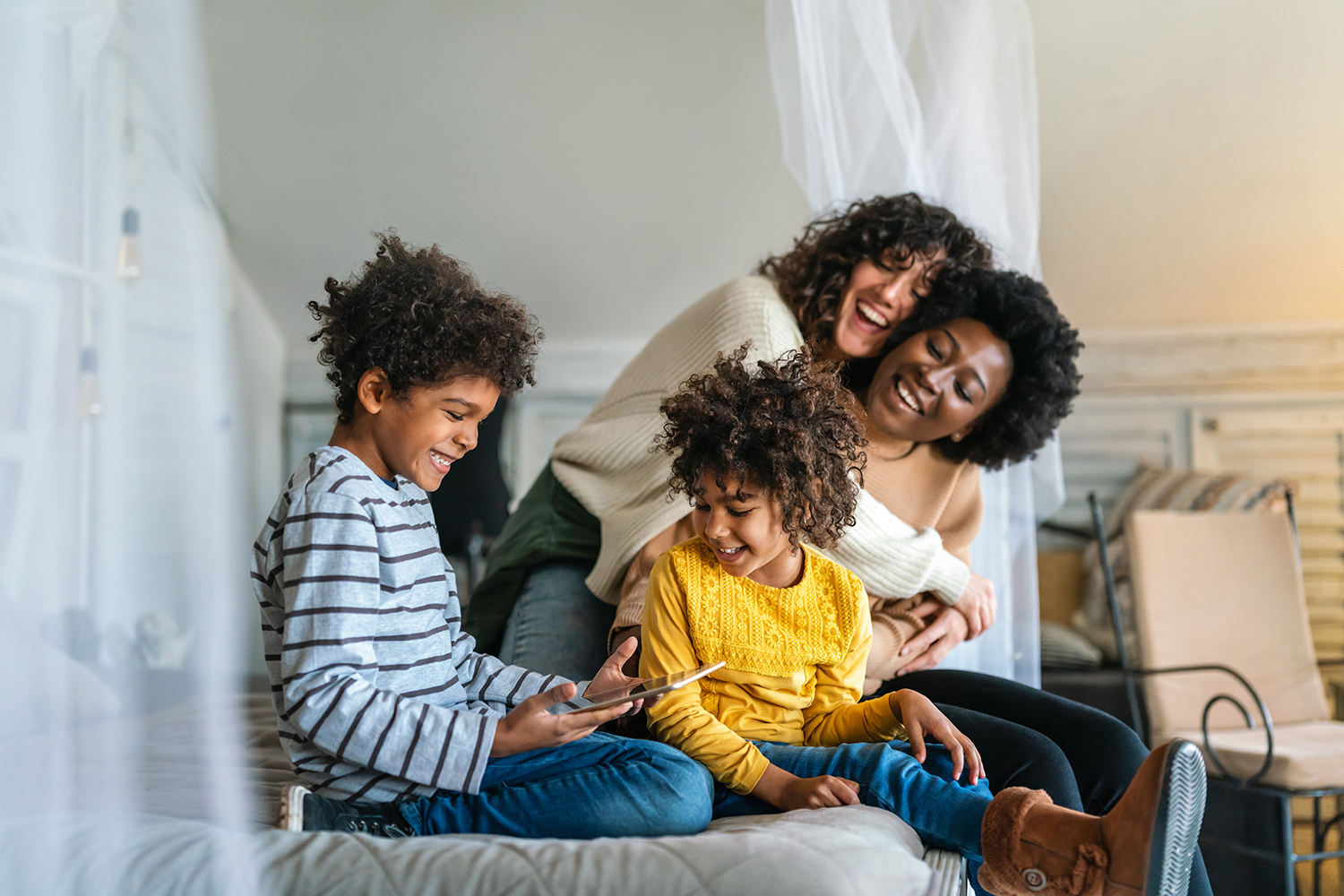 A family of two moms and two children, reading a book on a couch.