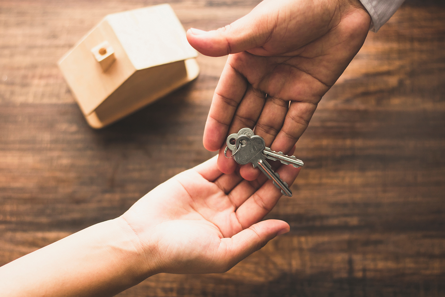 A person passing house keys to another person, over a wooden desk.